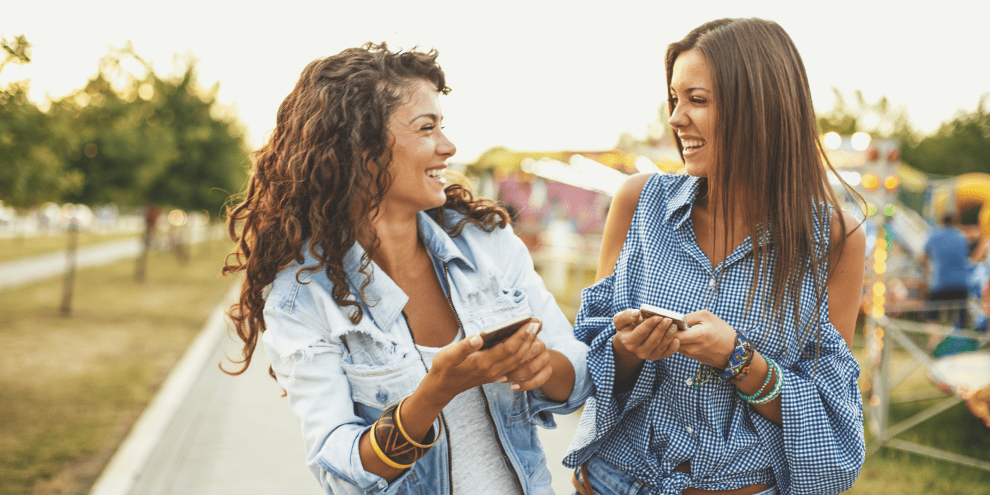 two ladies walking a carnival laughing while holding smartphones