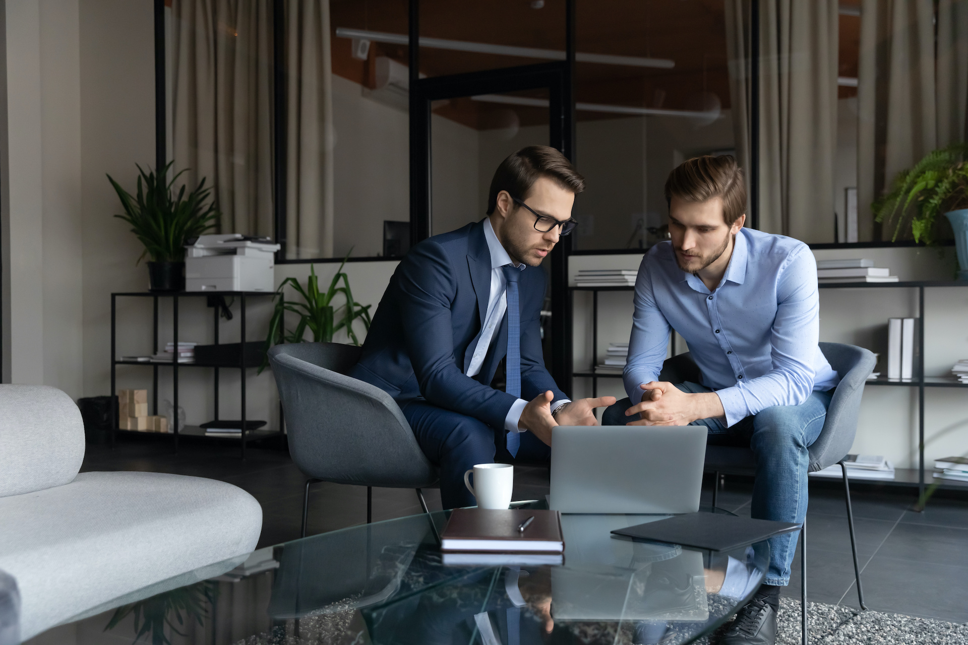 Serious male colleagues cooperate discuss ideas using laptop