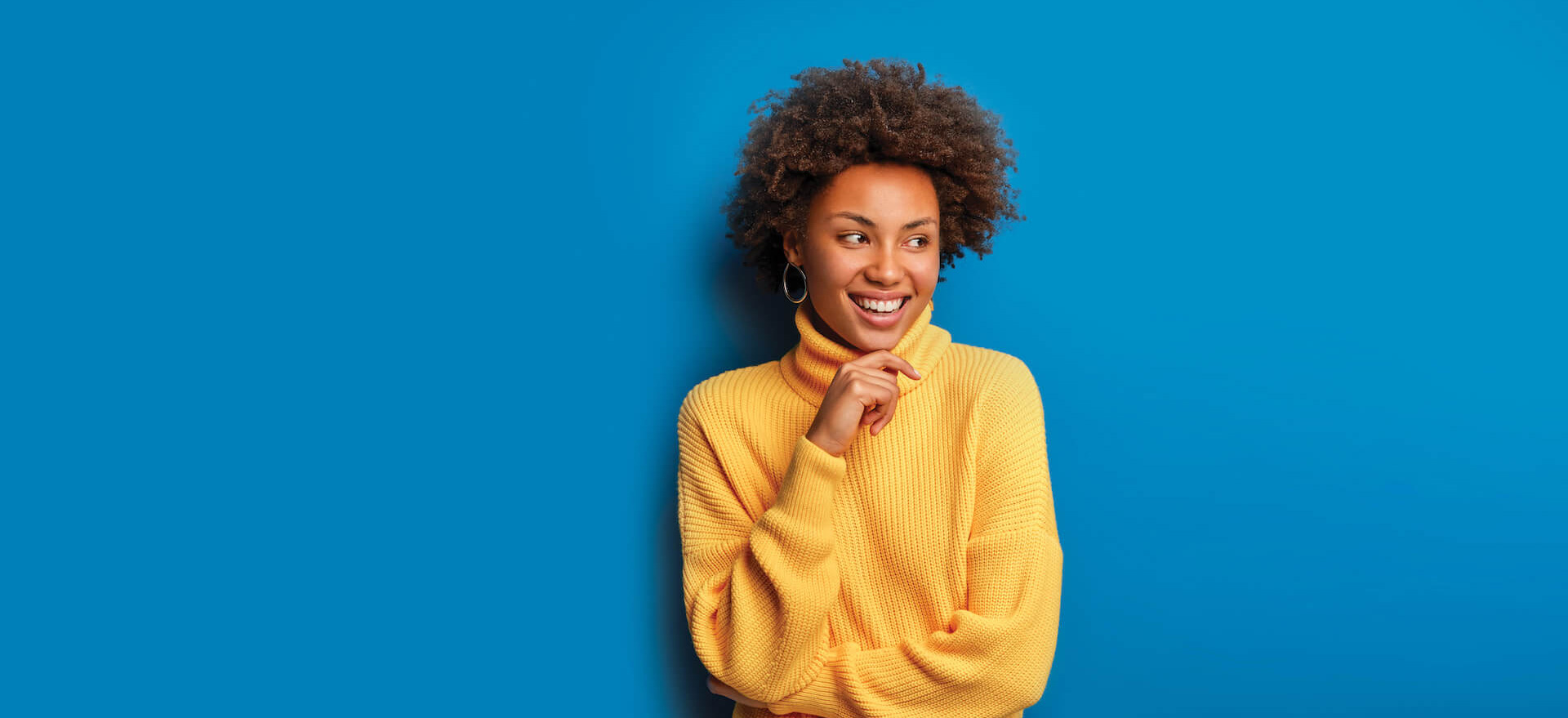 Woman standing infront of blue background in yellow sweater smiling