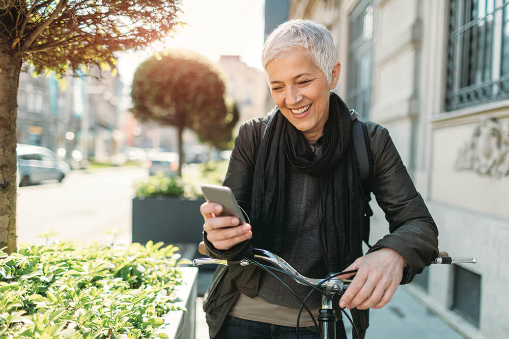 woman with bicycle stopped looking at smartphone smiling