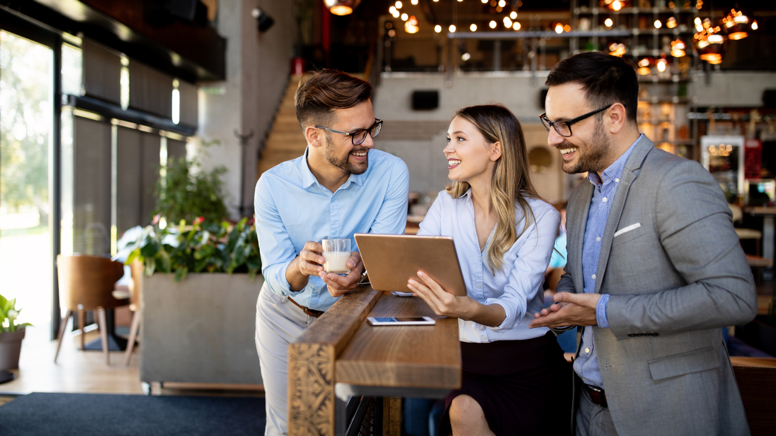 three business team members chat while looking at tablet.