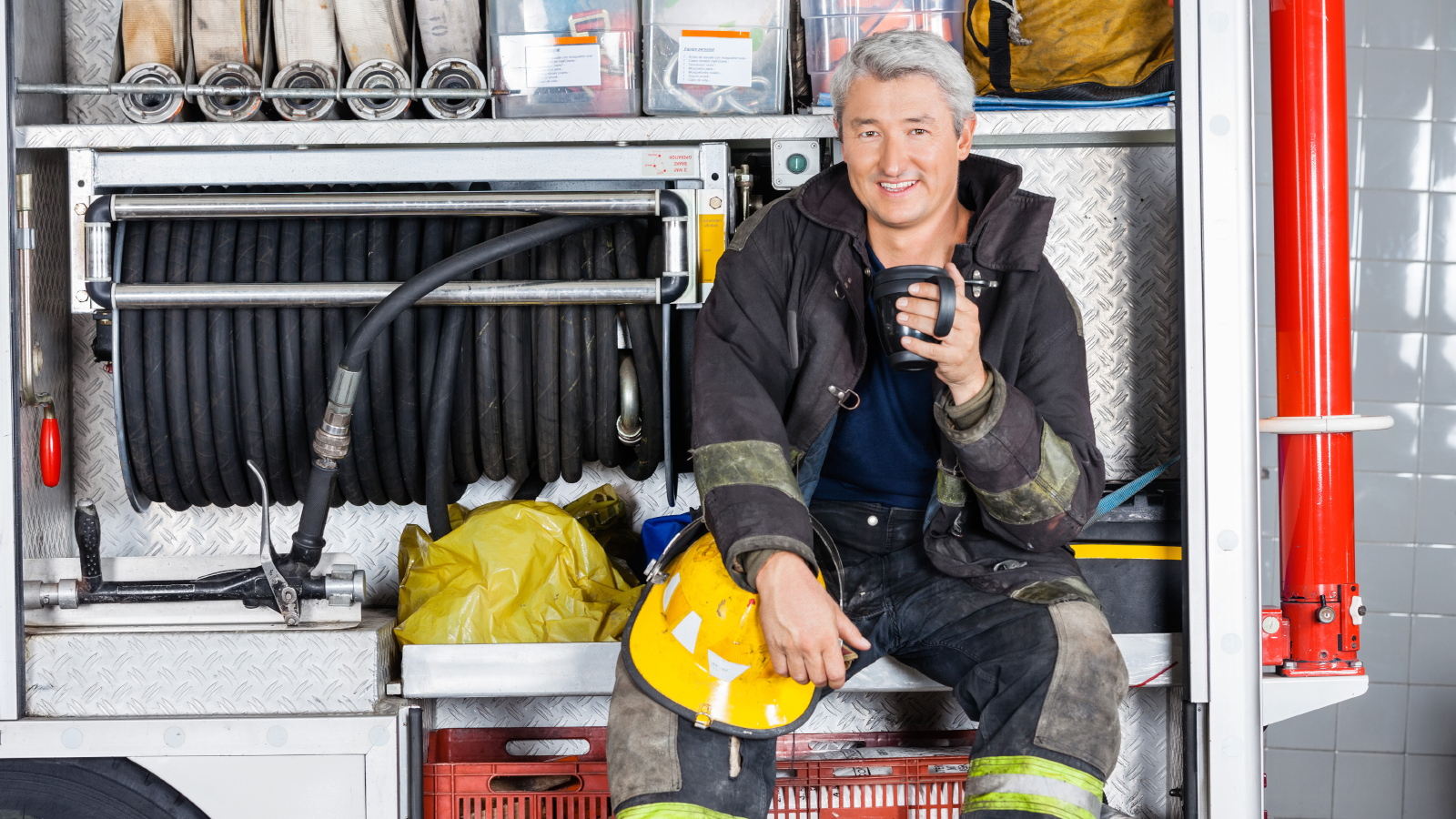 Firefighter relaxing on firetruck while drinking coffee