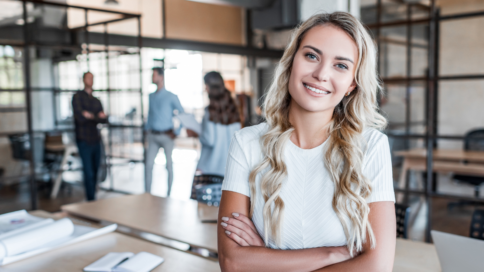 business woman standing with arms crossed and team members in background