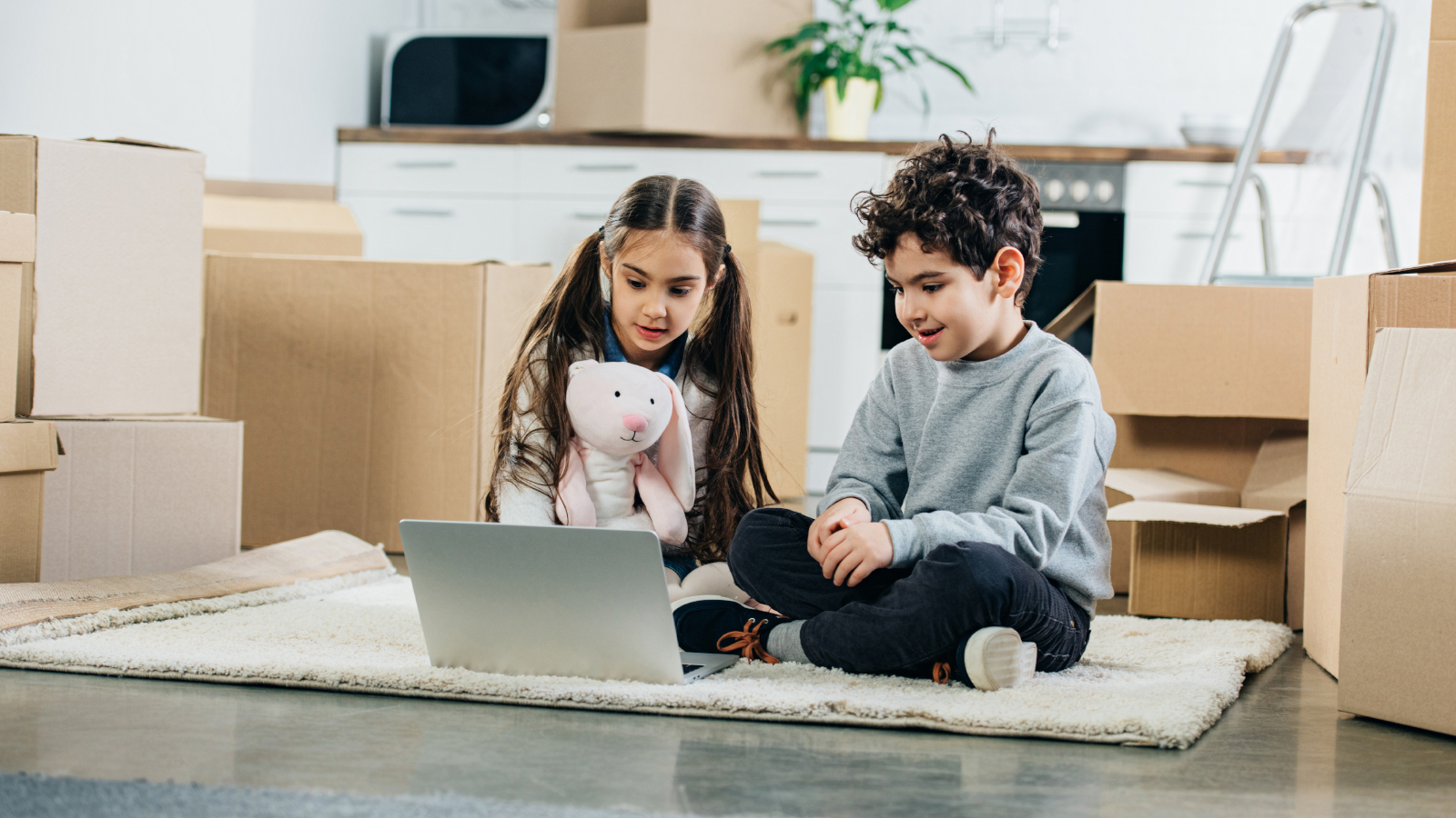 happy children using laptop while sitting on carpet in new home