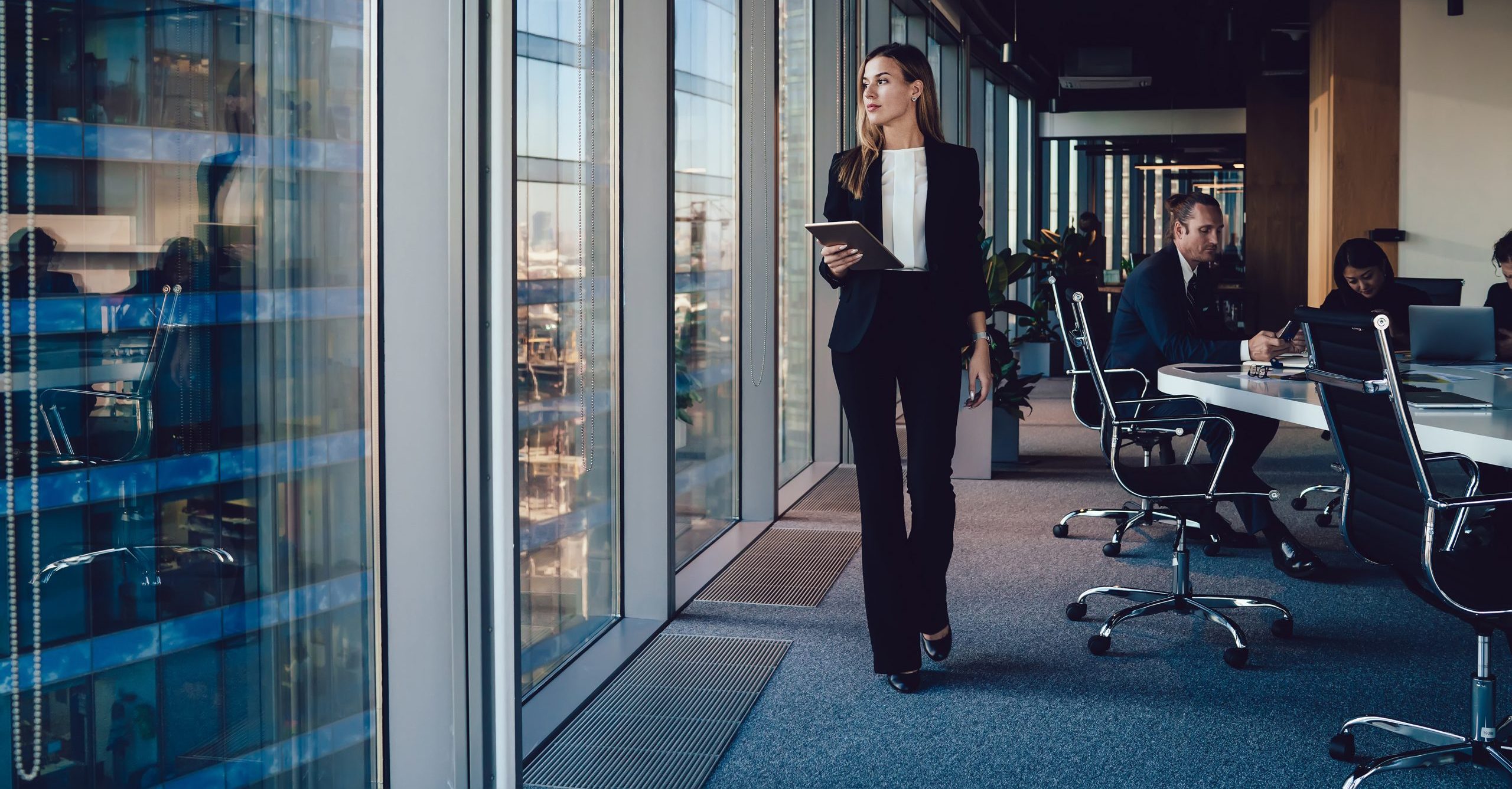 Businesswoman holding tablet in office, looking out window.