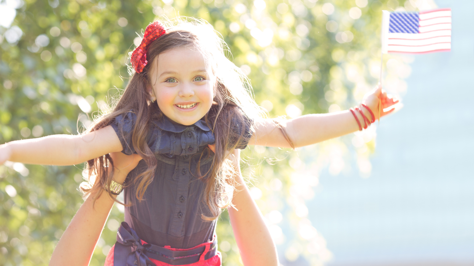 Little girl being held in the air while holding an American Flag.